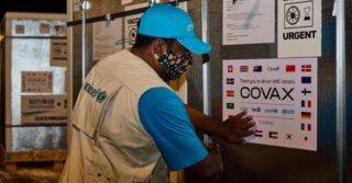 UNICEF worker with blue Unicef cap and beige vest puts up vaccination signage